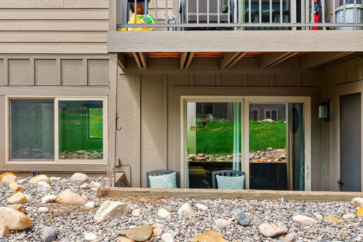 A peaceful outdoor setting featuring two chairs placed in front of large windows, surrounded by a landscaped area. The scene suggests a cozy spot for relaxation, reading, or sharing moments with a companion while enjoying the fresh mountain air.