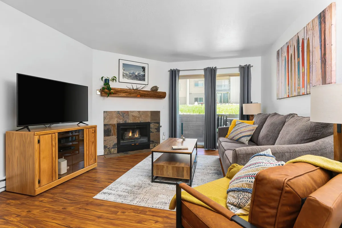 The image showcases the condo's inviting living area, featuring a cozy gas fireplace as the centerpiece, a comfortable sofa, a stylish coffee table, and vibrant artwork. The space exudes warmth, perfect for relaxing after a day on the slopes or gathering for a movie night with friends and family.