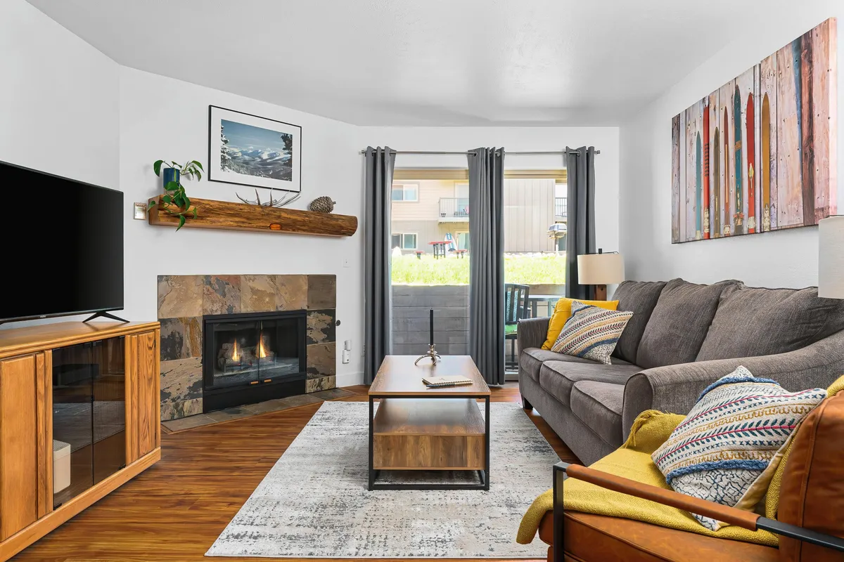 This image captures a warm, welcoming living room with a prominent fireplace, plush sofa, coffee table, and tasteful artwork on the wall. The seating is arranged to encourage conversation and relaxation, and the inviting atmosphere is enhanced by the glow of the fire.