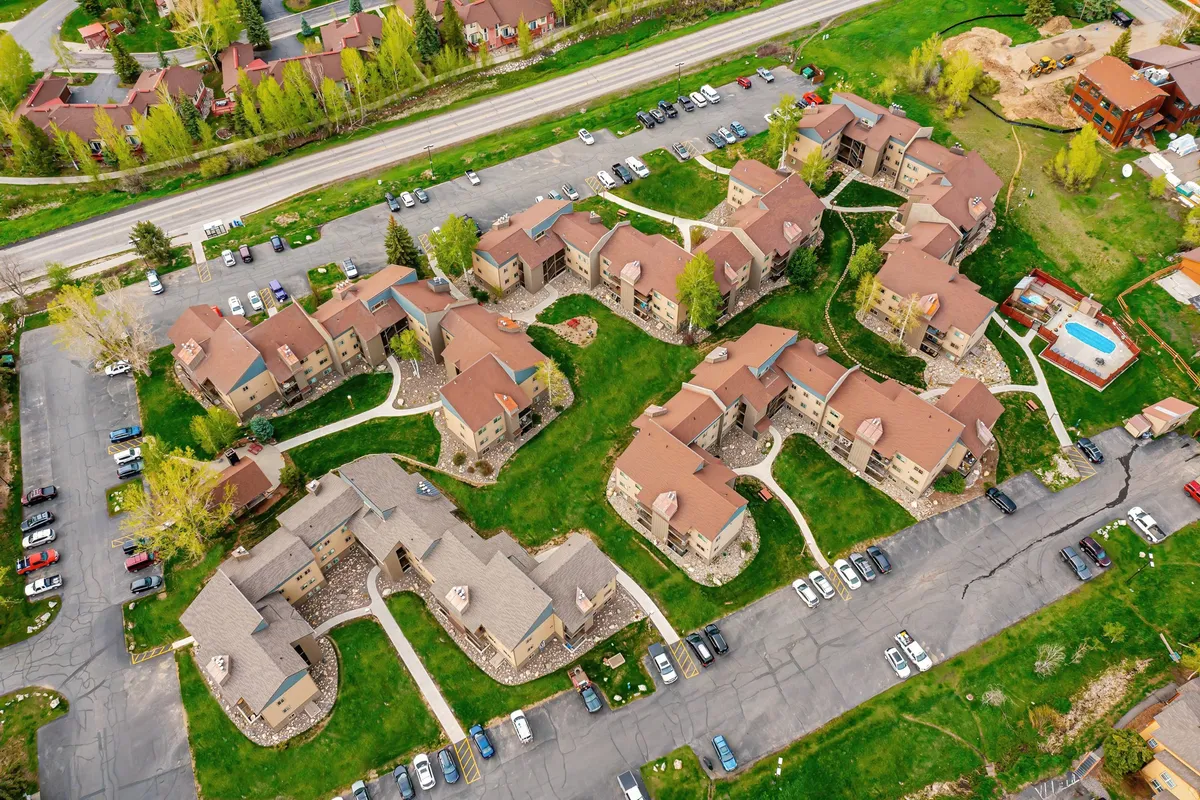 An exterior shot featuring multiple condo buildings with green lawns and a visible swimming pool area. The image conveys a sense of community, with open spaces perfect for gatherings and family relaxation during summer months.