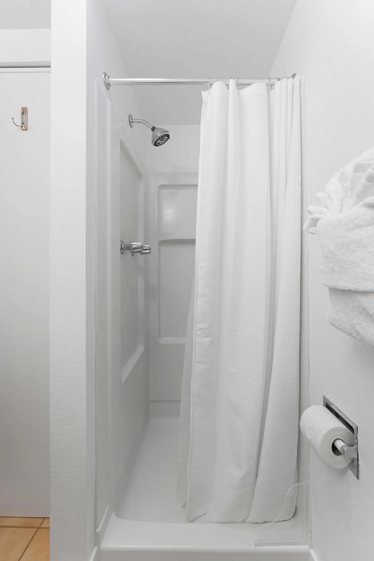 A tranquil bathroom scene featuring a shower with a curtain, showerhead, towel rack, and toilet paper holder. The space is neat, functional, and inviting, ideal for unwinding after a long day.