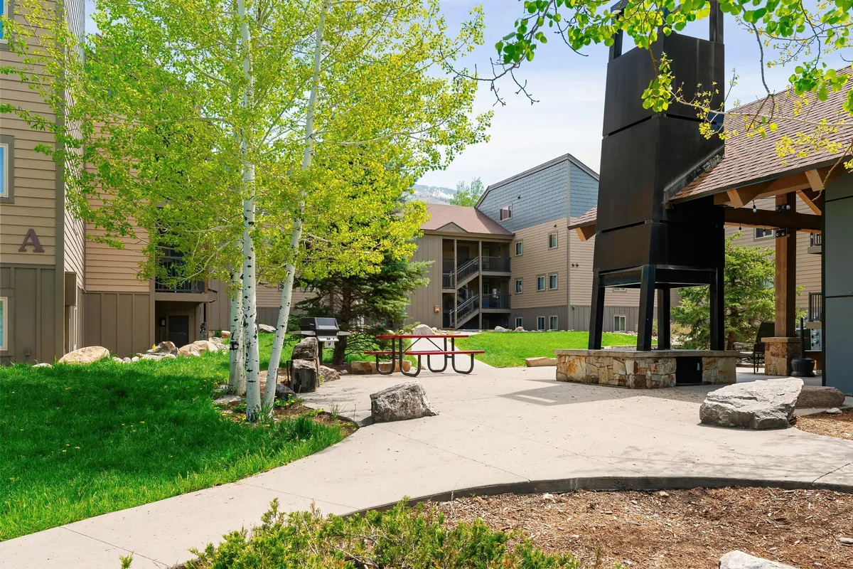 This exterior scene highlights green trees, striking rock formations, and a cheerful picnic area set against the community’s architecture. The atmosphere is lively yet peaceful, depicting a space perfect for picnics, social gatherings, or quiet moments in nature.