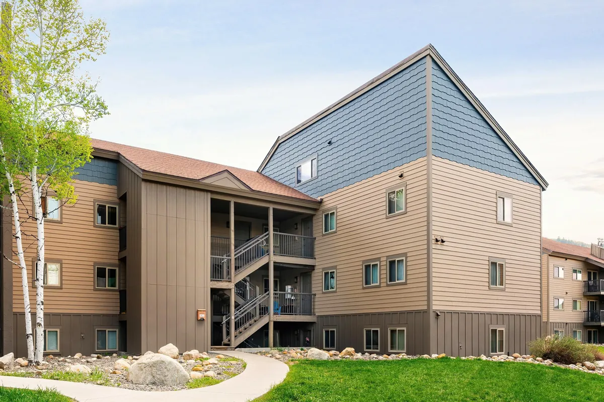 An exterior view focuses on a staircase, building facade, landscaped path, and surrounding greenery. The scene exudes a sense of coming and going, ideal for capturing the arrival and departure vibe of ski days.
