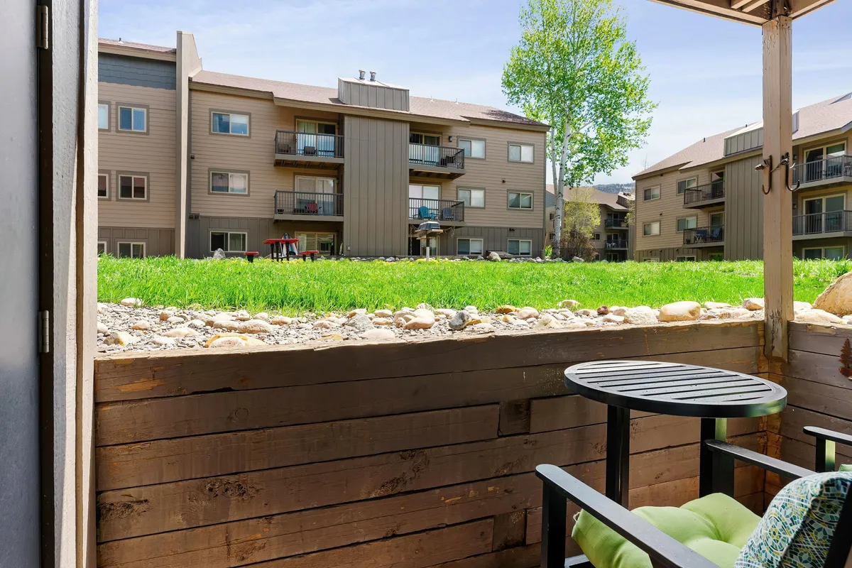 The image features a peaceful patio area with lush green grass, balconies, and wooden railings. It suggests a direct connection from the indoor living area to the outdoors, inviting fresh mountain air and moments of relaxation outside.