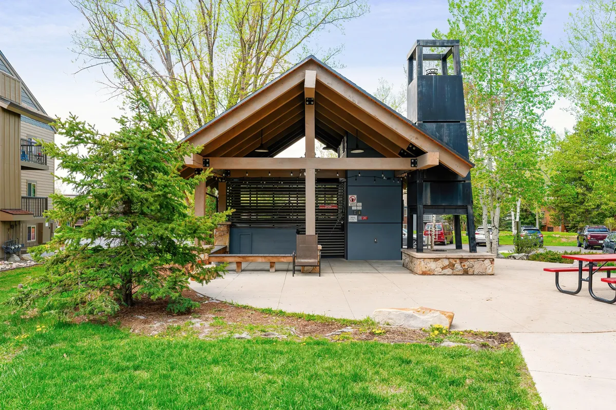 A welcoming pavilion structure and picnic table are surrounded by lush greenery, inviting residents to gather for outdoor meals or community events. The setting suggests a hub for summer celebrations and spontaneous get-togethers.