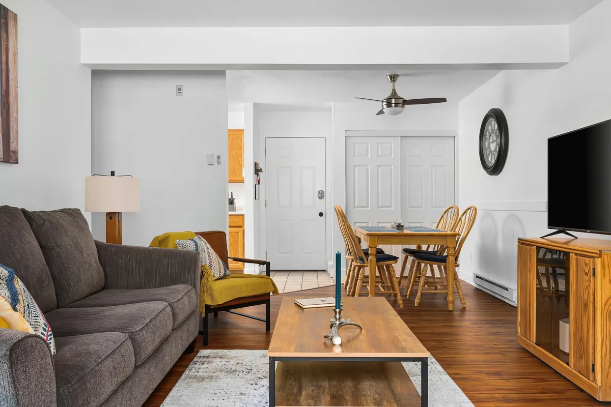 This scene shows an open-concept living area with a cozy sofa, coffee table, dining table, and a television. The space is clearly designed for both relaxation and entertaining, and its layout demonstrates the easy flow from living to dining that the section emphasizes.