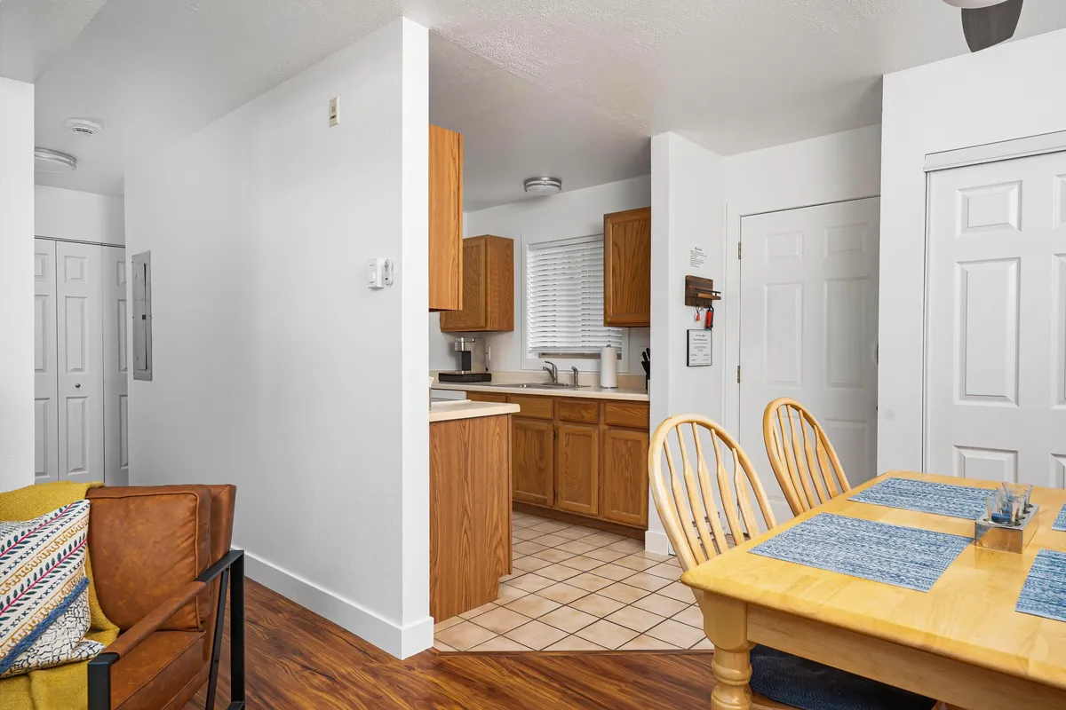 A welcoming open-concept space featuring a dining table at the center, a view into the kitchen area with modern appliances, and comfortable living room seating nearby. Natural light fills the area, highlighting the inviting ambiance ideal for family meals, cooking, and social gatherings.